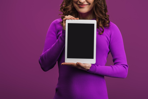 oříznutý pohled usměvavé ženy držící digitální tablet s prázdnou obrazovkou na fialovém pozadí - Fotografie, Obrázek