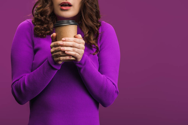 vista recortada de chica fría sosteniendo café para ir sobre fondo púrpura
 - Foto, imagen