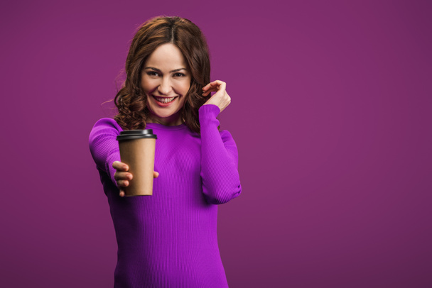 pretty girl smiling at camera while holding coffee to go on purple background - Photo, Image