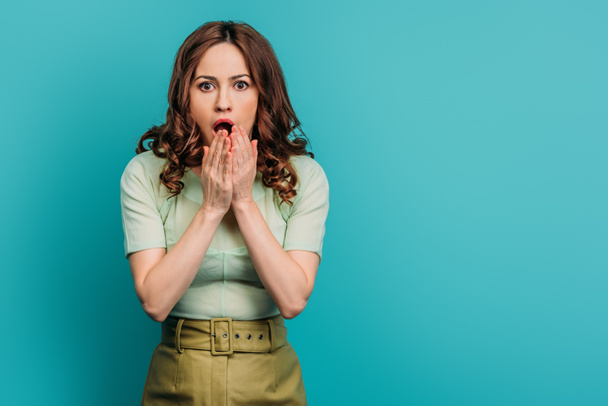 shocked woman holding hands near face while standing with open mouth on blue background - Фото, изображение