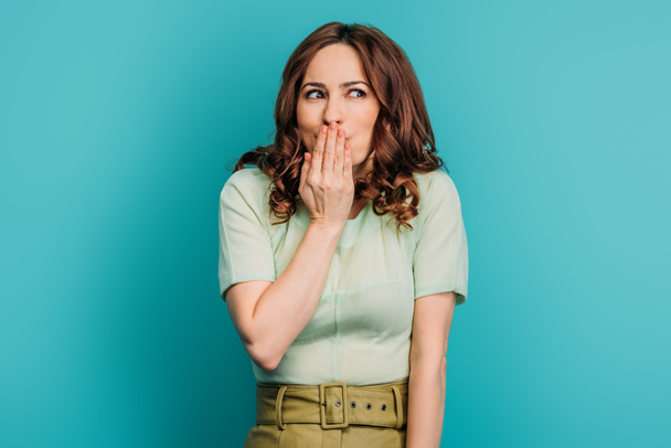 shocked girl looking away and covering mouth with hand on blue background - 写真・画像