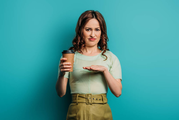 ontevreden vrouw tonen weigering gebaar terwijl het houden van koffie te gaan op blauwe achtergrond - Foto, afbeelding