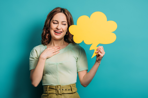 smiling woman holding hand on chest while holding thought bubble on blue background - Foto, imagen