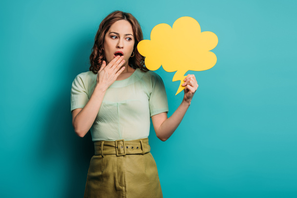 shocked woman holding hand near mouth while holding thought bubble on blue background - Photo, Image