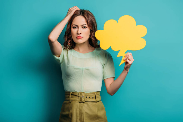 thoughtful woman touching head while holding thought bubble on blue background - Фото, изображение