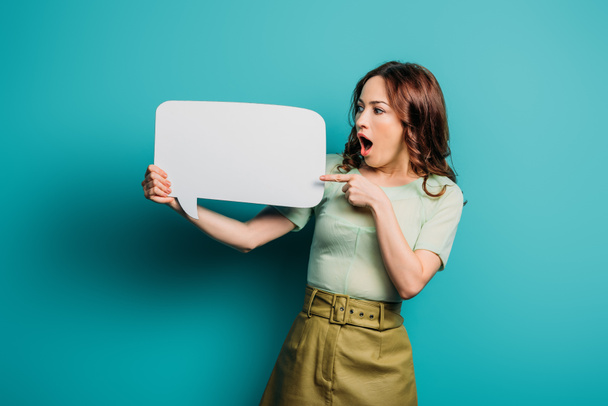 shocked woman pointing with finger at speech bubble on blue background - Photo, Image