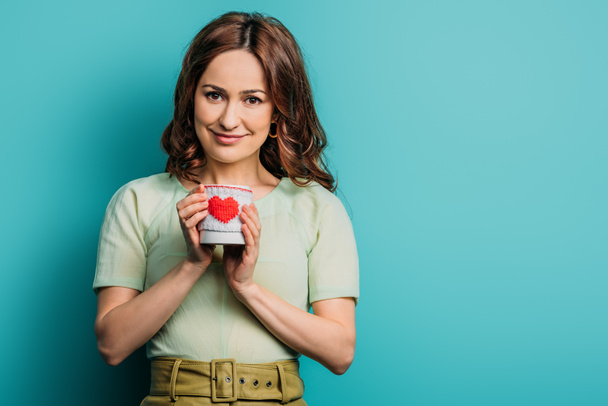 happy girl holding cup with heart symbol on blue background - Photo, Image