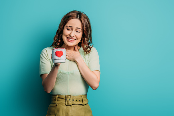 pleased girl holding cup with heart symbol on blue background - Φωτογραφία, εικόνα