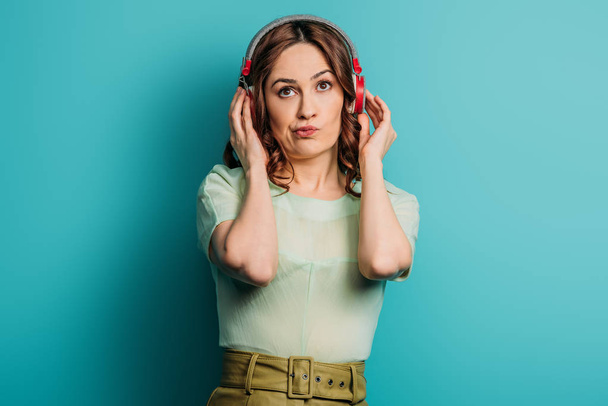 skeptical girl in wireless headphones looking up on blue background - Valokuva, kuva