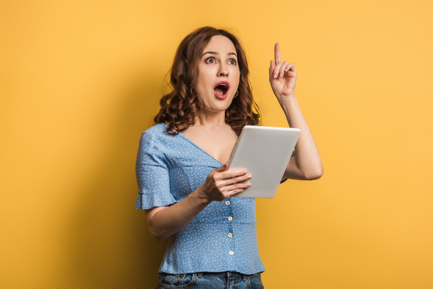 opgewonden vrouw tonen idee gebaar terwijl het houden van digitale tablet op gele achtergrond - Foto, afbeelding