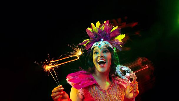 Beautiful young woman in carnival mask and masquerade costume in colorful lights, flyer - Foto, afbeelding