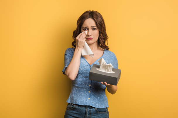 upset girl covering tears with paper napkin on yellow background - Photo, Image