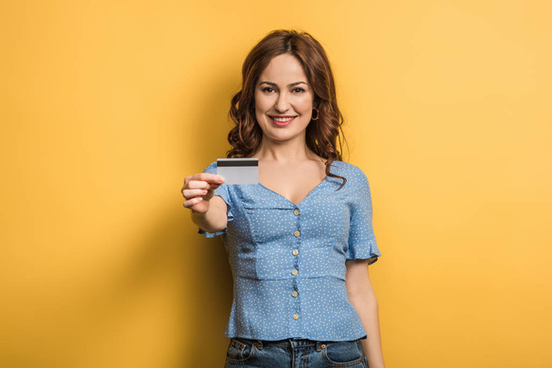happy young woman holding credit card on yellow background - Fotó, kép