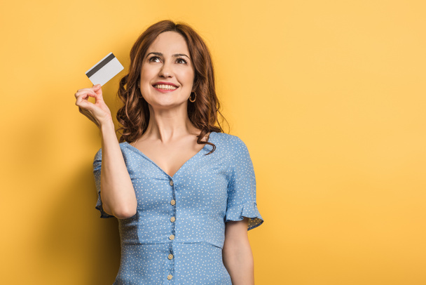 happy young woman holding credit card on yellow background - Foto, imagen