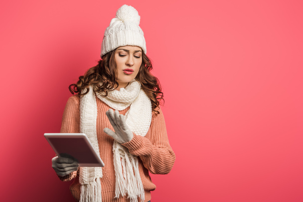 displeased girl in warm hat and scarf holding digital tablet and showing stop gesture on pink background - Φωτογραφία, εικόνα
