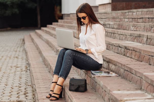 Портрет одной модной девушки, одетой в джинсы и белую рубашку, держащей ноутбук, внештатный работник, бизнес-леди, женщина Power Concept
 - Фото, изображение