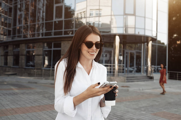 Portrét jedné módní dívka oblečené v džínách a bílé košile pití kávy a pomocí jejího smartphonu, obchodní dáma, žena Power Concept - Fotografie, Obrázek