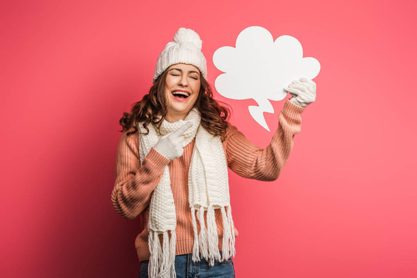 laughing girl in warm hat and scarf pointing with finger at thought bubble on pink background - 写真・画像