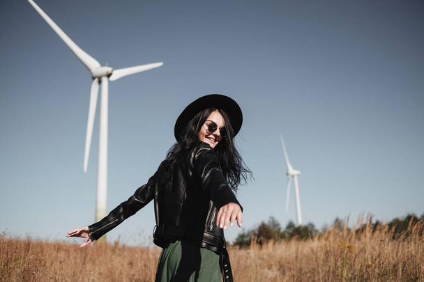 Happy Traveling Girl Enjoying a Trip on the Field Road with Electric Wind Turbine Power Generator on the Background - Photo, Image