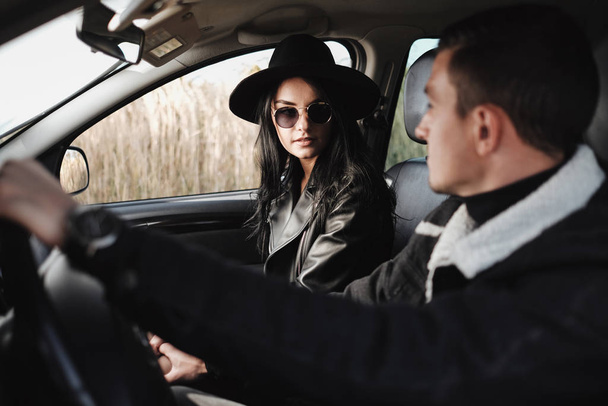 Щаслива подорожня пара одягнена в чорний стильний одяг насолоджуючись дорожньою поїздкою сидячи всередині автомобіля, концепція відпустки
 - Фото, зображення