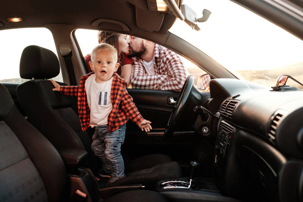 Happy Young Family Mom and Dad with Their Son Little Driver Enjoying Summer Weekend Picnic on the Car Outside the City in the Field at Sunny Day Sunset, Vacation and Road Trip Concept - Foto, imagen