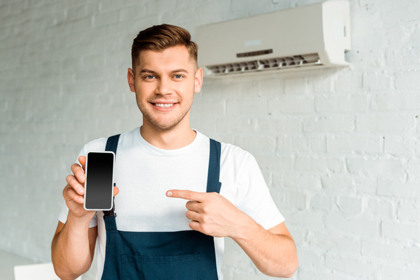cheerful installer pointing with finger at smartphone with blank screen  - Photo, Image
