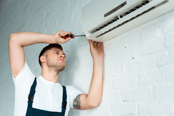 handsome tattooed installer holding screwdriver near air conditioner  - Photo, Image