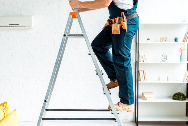 cropped view of installer in overalls climbing ladder  - Photo, Image