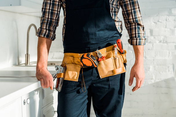 cropped view of installer with tool belt standing in kitchen  - Photo, Image