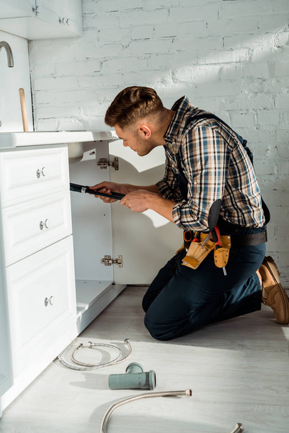 side view of installer standing on knees while working near kitchen cabinet  - 写真・画像