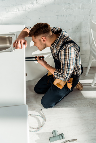 side view of installer holding slip joint pliers while working near kitchen cabinet  - Fotó, kép