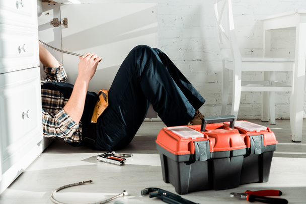 обрезанный вид инсталлятора, лежащего на полу возле ящика с инструментом
  - Фото, изображение