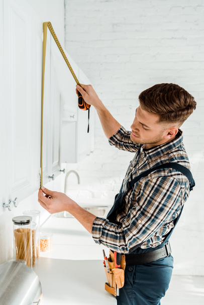 installer in overalls measuring white kitchen cabinet  - Foto, Imagem