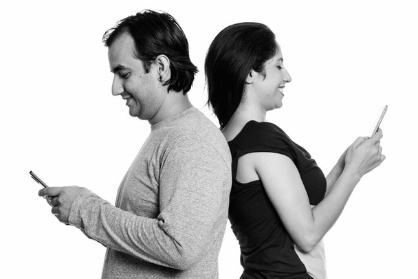Gelukkige Perzisch paar lacht tijdens het gebruik van mobiele telefoon samen rug aan rug - Foto, afbeelding
