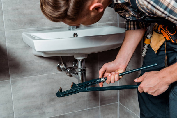selective focus of installer holding slip joint pliers near pipe in bathroom  - Foto, imagen