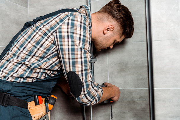 serious installer in overalls standing in bathroom near pipe  - Photo, Image