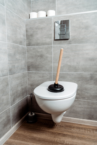 plunger on white toilet near toilet paper rolls  - Photo, Image