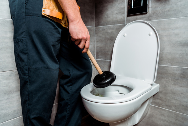 cropped view of plumber holding plunger near toilet  - Zdjęcie, obraz