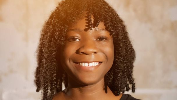Chica afroamericana con el pelo rizado mira hacia adelante y sonríe
 - Foto, Imagen