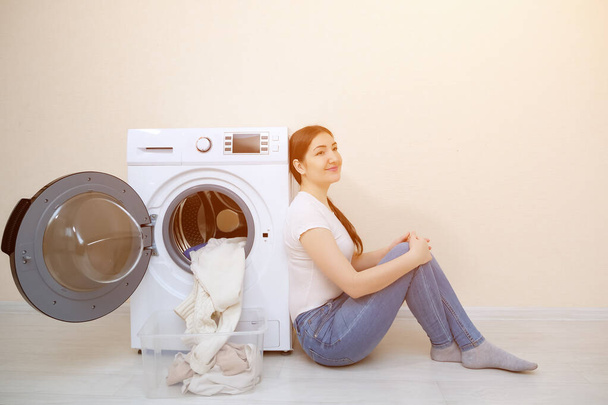 mujer sentada cerca de la lavadora con ropa limpia
 - Foto, imagen