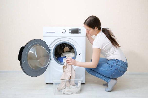 woman loads dirty clothes into washer near beige wall - Foto, immagini