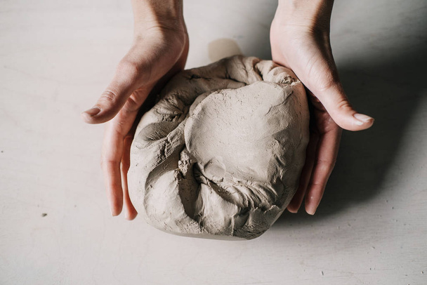 Female potter hands working with clay in workshop. White desk on background - Foto, afbeelding