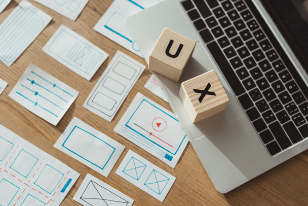 Hoge hoek weergave van kubussen met ux letters op laptop met website wireframe schetsen op houten tafel - Foto, afbeelding