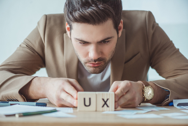 Selectieve focus van knappe ontwerper kijken naar kubussen met ux letters aan tafel - Foto, afbeelding