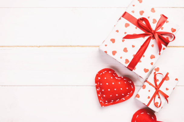 Valentin ou autre cadeau de vacances fait à la main en papier avec des cœurs rouges et une boîte cadeau dans un emballage de vacances. Cadeau cadeau boîte cadeau sur table en bois blanc vue de dessus avec espace de copie, espace vide pour la conception
 - Photo, image
