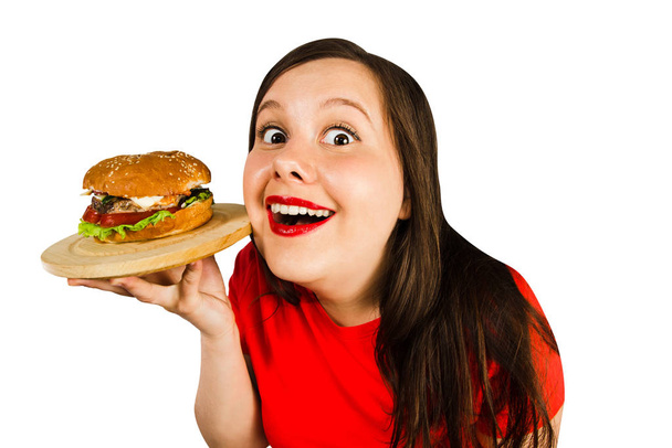 Young fat woman holds hamburger, smiles with opened mouth isolated on white background. - Foto, Imagen