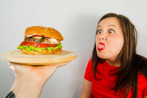 Young girl refuses fat unhealthy hamburger because she is losing weight and dieting on gray background. - Foto, Imagen