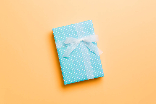 csomagolva karácsony vagy más ünnep kézzel készített ajándék papír fehér szalaggal narancssárga alapon. Jelen doboz, díszítés ajándék színes asztalon, felülnézet másolási hellyel - Fotó, kép