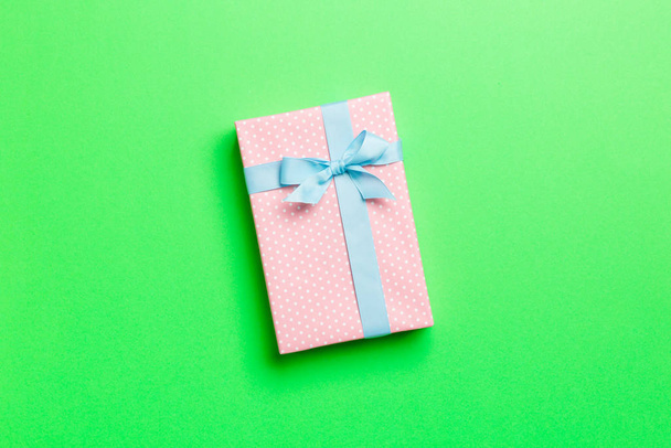 wrapped Christmas or other holiday handmade present in paper with blue ribbon on green background. Present box, decoration of gift on colored table, top view with copy space - Foto, imagen