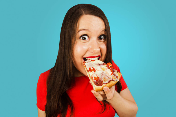 Νεαρή όμορφη γυναίκα τρώει πίτσα, σε μπλε φόντο. Πλευρική άποψη. - Φωτογραφία, εικόνα